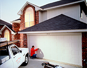 Garage door technician inspecting a white two-car garage door on a large brick home.
