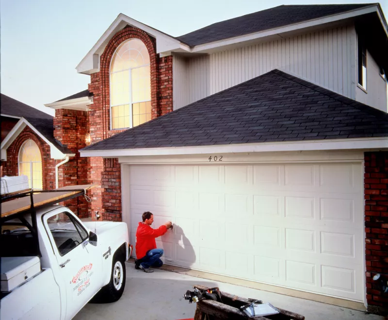 Technician inspecting a white garage door on a large brick home.