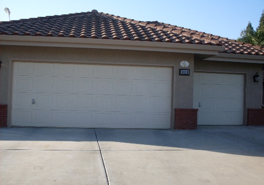 Two white paneled garage doors on a home with tile roofing.
