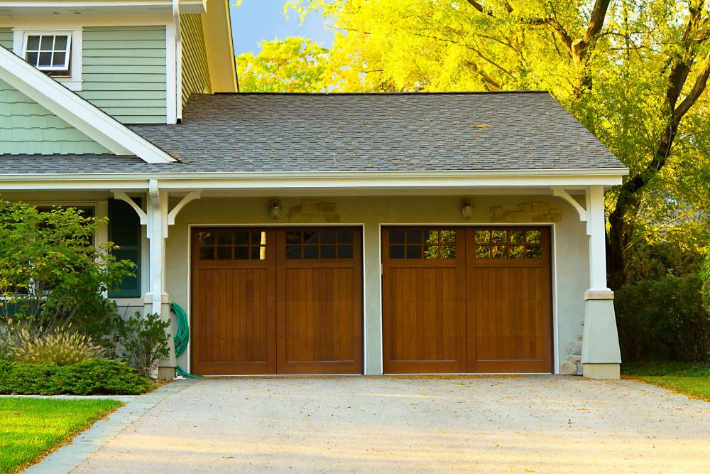 Modern wood-grain two-car garage doors with small windows in the top, on a home with light green siding.